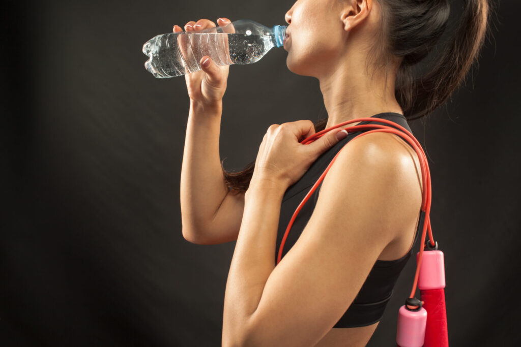 Eine sportliche Frau mit Springseil trinkt nach dem Training erfrischendes Wasser aus einer Flasche.