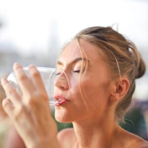 Eine Frau trinkt mit geschlossenen Augen genussvoll ein Glas klares Wasser, das durch einen Wasserfilter aufbereitet wurde.