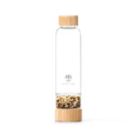 Wiederverwendbare Glasflasche von Lotus Vita mit Bambusdeckel und -boden, wobei der Boden eine separate Kammer mit gold-braunen Edelsteinen enthält.
