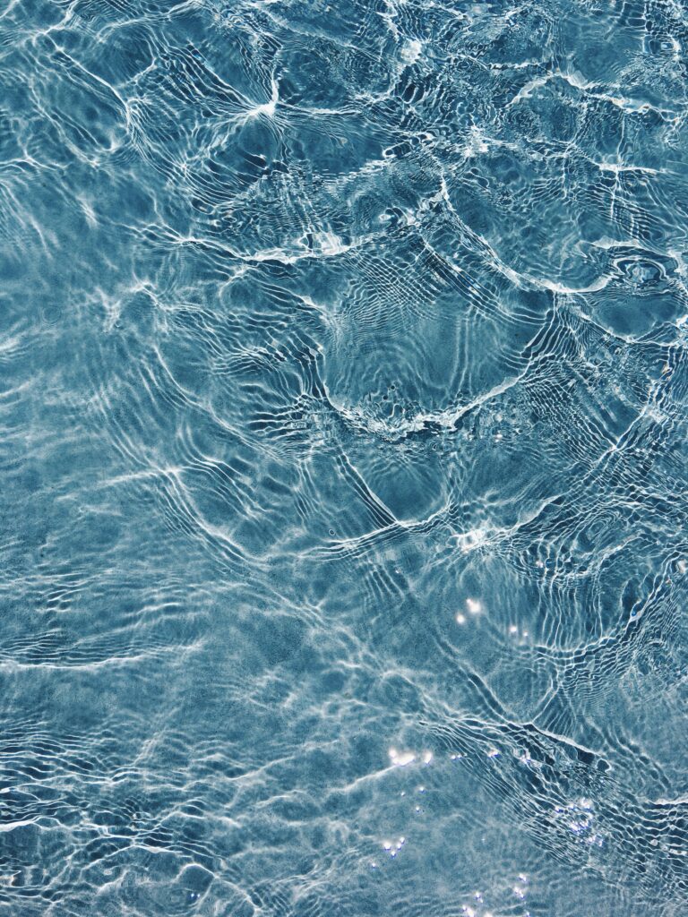 Klares, blaues Wasser, dessen Oberfläche von sanften Wellen und Lichtreflexen durchzogen ist.