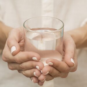 Eine Frau in einem weißen Hemd hält mit beiden Händen ein Glas mit klarem, reinem Wasser.